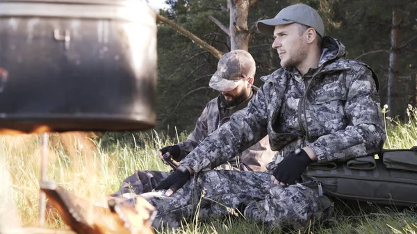 Two young man hunters near forest. Summer vacation forest. Friends sit at forest picnic. Best friends spend leisure weekend hike barbecue forest nature background. Make fire in nature.