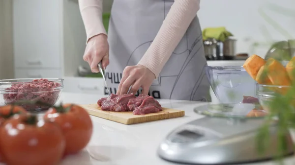 Woman cutting raw meat on small pieces with kitchen knife cutting board. Female cutting red beef filet on wooden board, holding knife in hand. Housewife is cooking at home interior. Concept: food