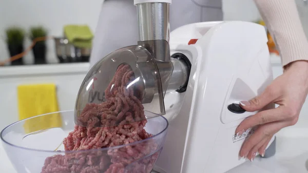 Making minced meat in electric meat grinder from fresh beef at home. Electric mincer machine with fresh chopped meat. Preparation of minced beef with electric grinder. Written on apron: best recipes