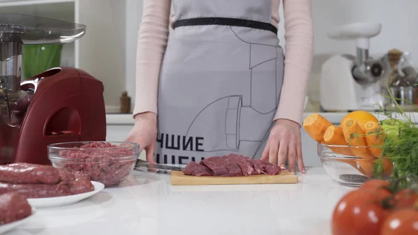 Woman cutting raw meat on small pieces with kitchen knife cutting board. Female cutting red beef filet on wooden board, holding knife in hand. Housewife is cooking at home interior. Concept: food
