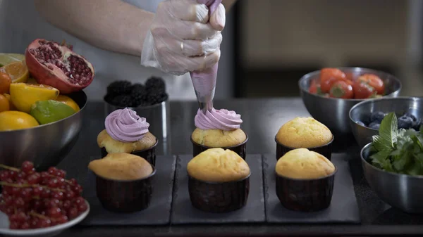 Decorating cup cake with cream. Using cooking bag, confectioner making muffins. Modern desserts and cakes. Cupcakes with cream filling. Professional pastry. Stock Picture