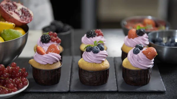 Cupcakes with cream filling. Decorating with mint, strawberry and blueberry. Modern desserts and cakes. Cupcakes with cream filling. Professional pastry. Stock Picture