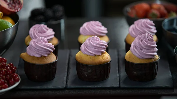 Decorating cup cake with cream. Using cooking bag, confectioner making muffins. Modern desserts and cakes. Cupcakes with cream filling. Professional pastry. Stock Picture