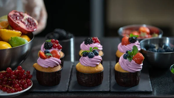 Cupcakes with cream filling. Decorating with mint, strawberry and blueberry. Modern desserts and cakes. Cupcakes with cream filling. Professional pastry. Stock Photo