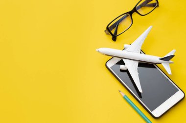 Gözlüklü uçak ve seyahat rezervasyonu konseptinde sarı arka planda kalemli akıllı telefon.