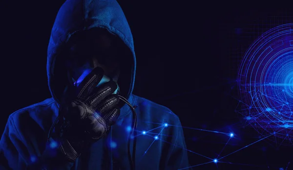 bad guy hacker with blue hood outfit and mask with glove on dark background in security virus network concept