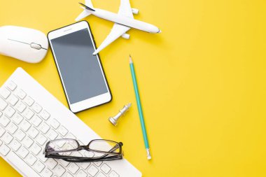 Dünya Tur rezervasyon konsepti etrafında seyahat sarı arka planda beyaz klavye ile kalem ile gözlük ve akıllı telefon ile üst görünüm uçak