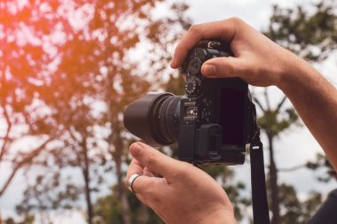 Adam fotoğraf çekmek için kamera tutuyor. Orman manzarası arka planı, macera turizmi, sırt çantasıyla dağlara seyahat.