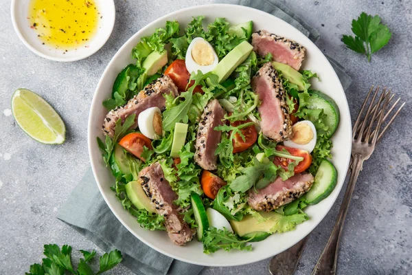 grilled tuna, avocado, tomato and egg salad in white bowl, top view