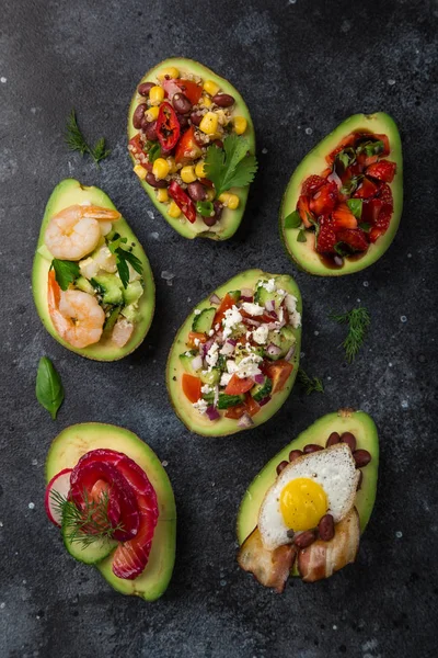 Avocado Helften Gevuld Met Verschillende Toppings Donkere Achtergrond Bovenaanzicht — Stockfoto