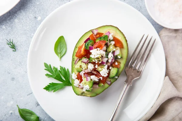 avocado stuffed with tomato, cucumber and feta cheese on white plate, top view,