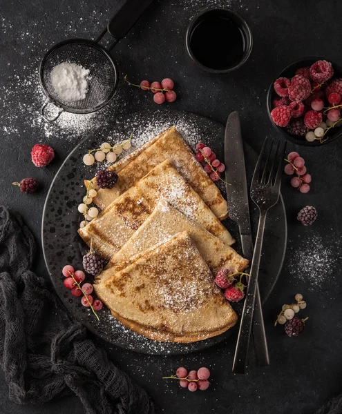 crepes with  frozen berries and powdered sugar, top view, dark background, square image