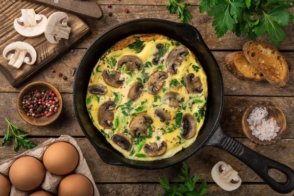 omelette with mushrooms on cast iron pan, top view, wooden background
