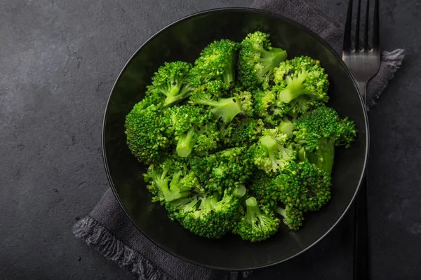 steamed broccoli with sesame seeds in black bowl, dark background, top view