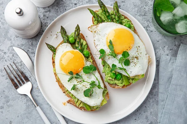 Toasts with avocado, asparagus and fried egg on white plate — Stock Photo, Image