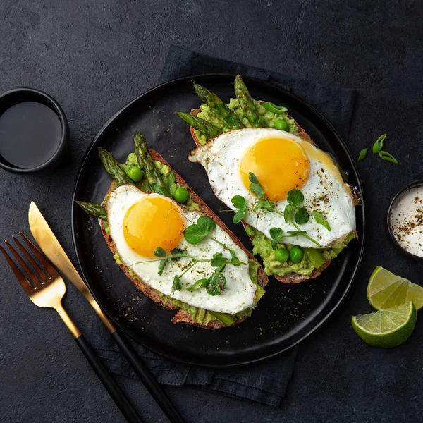 Tostadas Con Aguacate Espárragos Huevo Frito Plato Negro Vista Superior —  Fotos de Stock