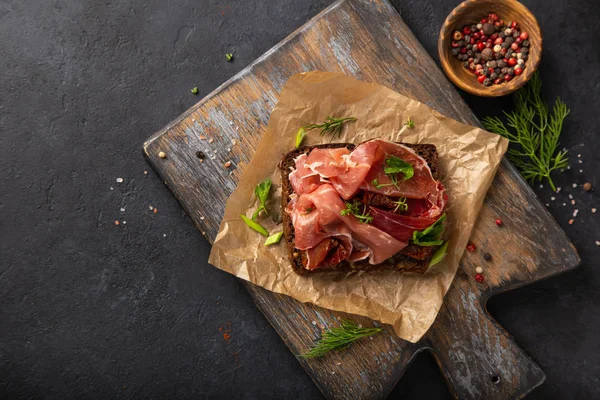 Nyitott sanwich sötét rozskenyér, prosciutto és a nap szárított Ástút — Stock Fotó