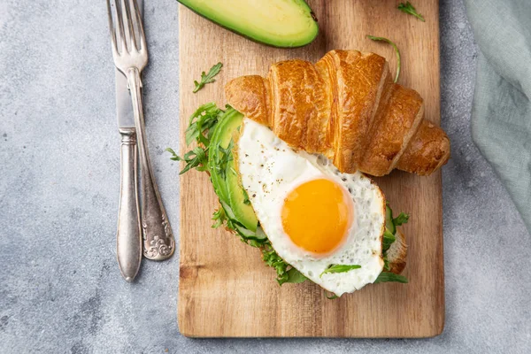 Бутерброд с круассаном с авокадо, жареным яйцом и рукколой на перерыв — стоковое фото