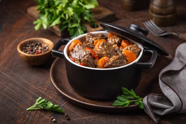 Beef stew with vegetables in black pot on dark wooden background — Stock Photo, Image