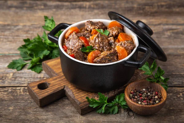 Beef stew with vegetables in black pot on dark wooden background — Stock Photo, Image