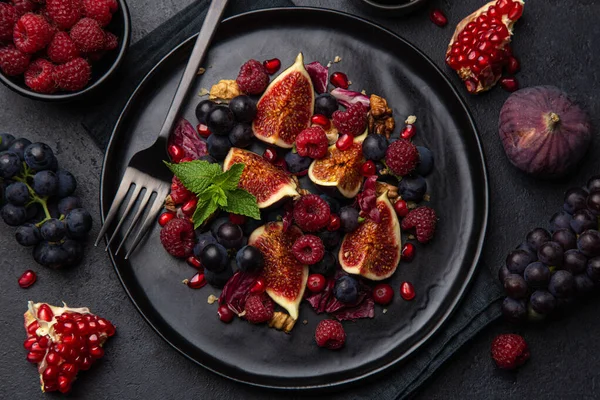 Feigen, Trauben, Himbeeren und Granatapfel Salat auf schwarzem Teller — Stockfoto