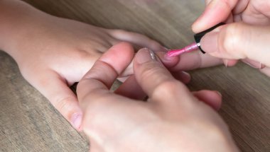 Pembe oje üzerinde küçük bir kız çivi koyar bir kadının elleri.