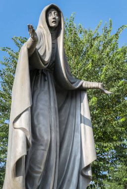 Meryem Ana heykeli bronz, mavi gökyüzü arka plan beyaz bulutlar ve ağaç, uzanmış kollarıyla.