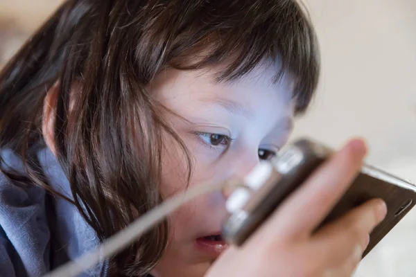 Cute young child watching screen of smartphone closely. Digital device addiction, childhood and education. Shallow dof.