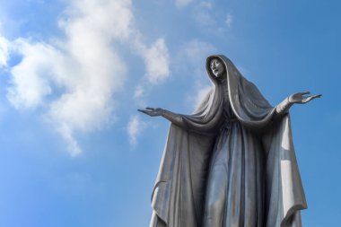 Meryem Ana heykeli bronz, mavi gökyüzü arka plan beyaz bulutlar, uzanmış kollarıyla ile.