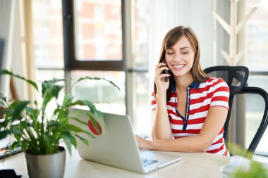 Genç kadın ofiste dizüstü bilgisayar ile masada otururken Smartphone'da söz 