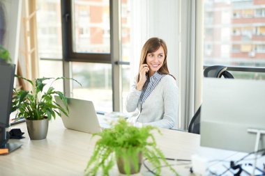 Genç kadın ofiste dizüstü bilgisayar ile masada otururken Smartphone'da söz 