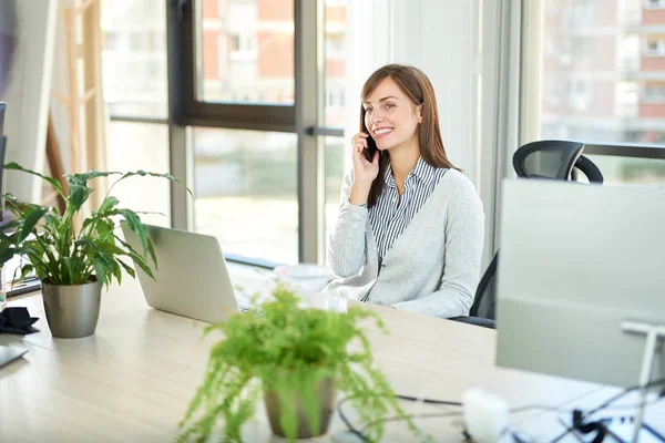 Genç kadın ofiste dizüstü bilgisayar ile masada otururken Smartphone'da söz 