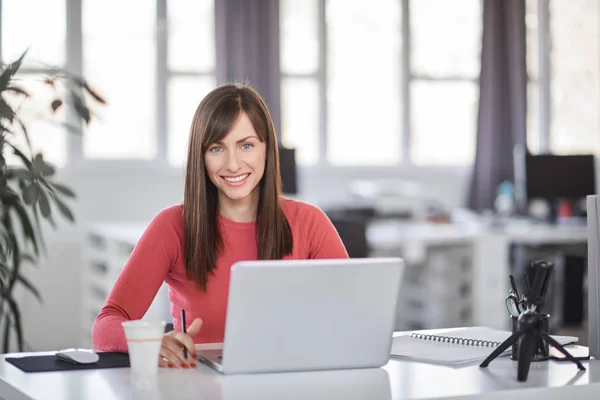 Bella donna d'affari caucasica sorridente seduta in ufficio moderno e utilizzando il computer portatile . — Foto Stock