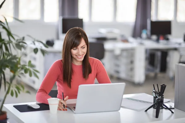 Hermosa mujer de negocios caucásica sonriente sentada en la oficina moderna y usando el ordenador portátil . — Foto de Stock