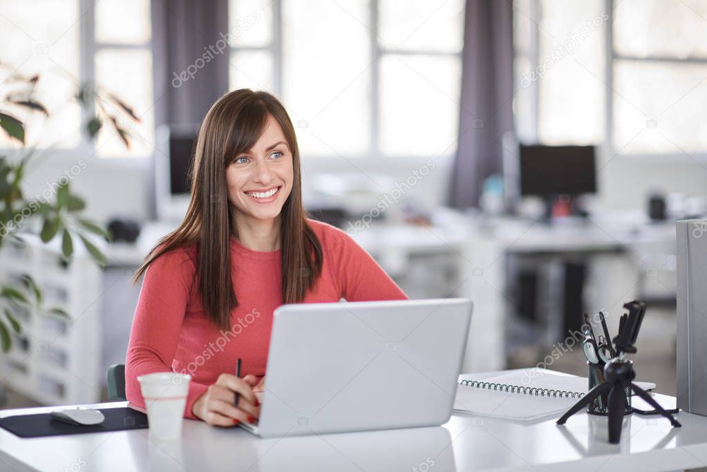 Beautiful smiling Caucasian businesswoman sitting in modern office and using laptop.