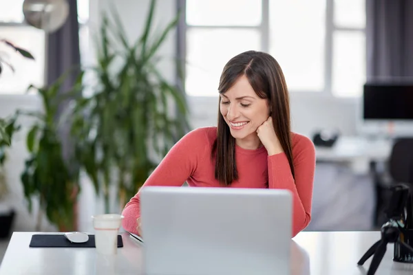 Charming Caucasian businesswoman sitting in modern office and taking notes in notebook. In front of her laptop. — Stock Photo, Image