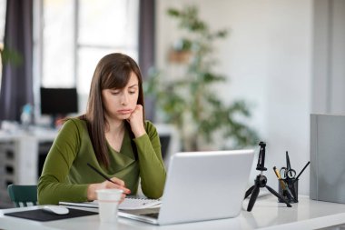 Moderna ofis ve not defterindeki not almak oturan sevimli beyaz iş kadını. Onu laptop önünde.
