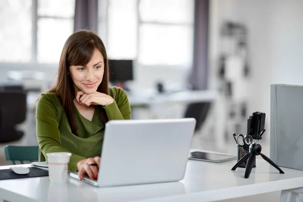 Hermosa mujer de negocios caucásica sonriente sentada en la oficina moderna y usando el ordenador portátil . — Foto de Stock