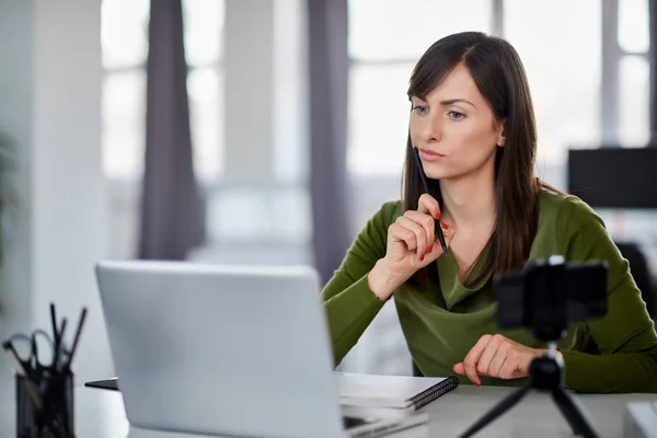 Beautiful serious Caucasian businesswoman sitting in modern office and using laptop. — Stock Photo, Image