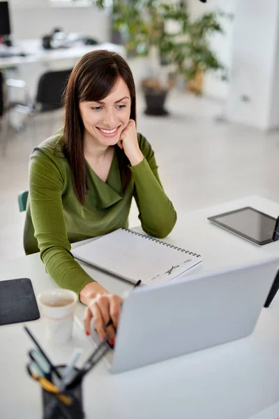 Bonita mulher de negócios caucasiana sorridente sentada no escritório moderno e usando laptop . — Fotografia de Stock