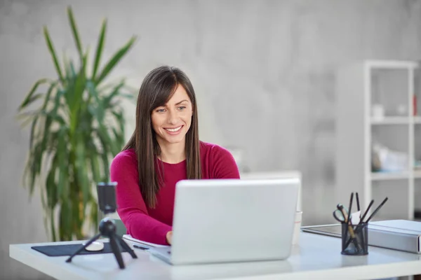 Bonita mulher de negócios caucasiana sorridente sentada no escritório moderno e usando laptop . — Fotografia de Stock