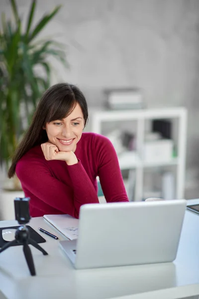 Bonita mulher de negócios caucasiana sorridente sentada no escritório moderno e usando laptop . — Fotografia de Stock