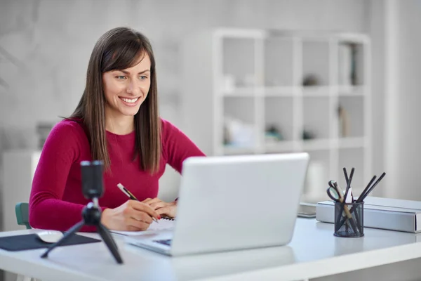 Beautiful smiling Caucasian businesswoman sitting in modern office and writing notes in notebook. — Stock Photo, Image