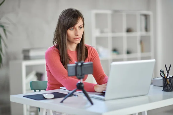 Beautiful serious Caucasian businesswoman sitting in modern office and using laptop. — Stock Photo, Image