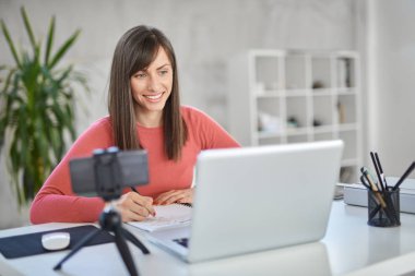 Modern ofis ve not defterindeki not almak oturan sevimli beyaz iş kadını. Onu laptop önünde.