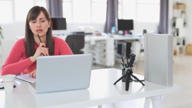 Young beautiful Caucasian businesswoman with brown hair sitting in office and using laptop.