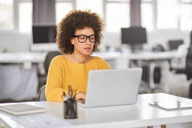 Ciddi karışık ırk iş kadını modern ofiste oturan ve dizüstü bilgisayar kullanarak rahat giyinmiş.