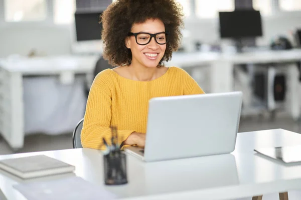 オフィスに座ってラップトップを使用してカジュアルな服を着た美しい笑顔の混合レースビジネスウーマン. — ストック写真