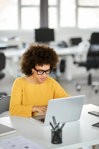 Schöne lächelnde gemischte Rasse Geschäftsfrau lässig gekleidet im Büro sitzend und mit Laptop. — Stockfoto