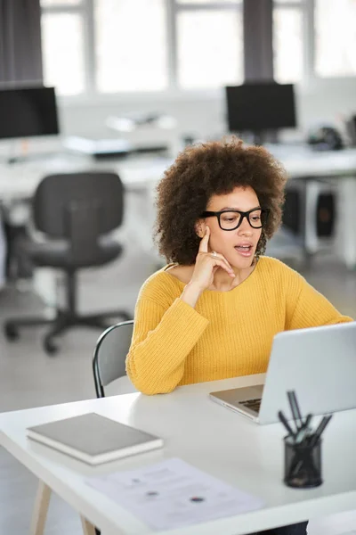 Linda mulher de negócios de raça mista sorridente vestida casual sentada no escritório e usando laptop . — Fotografia de Stock